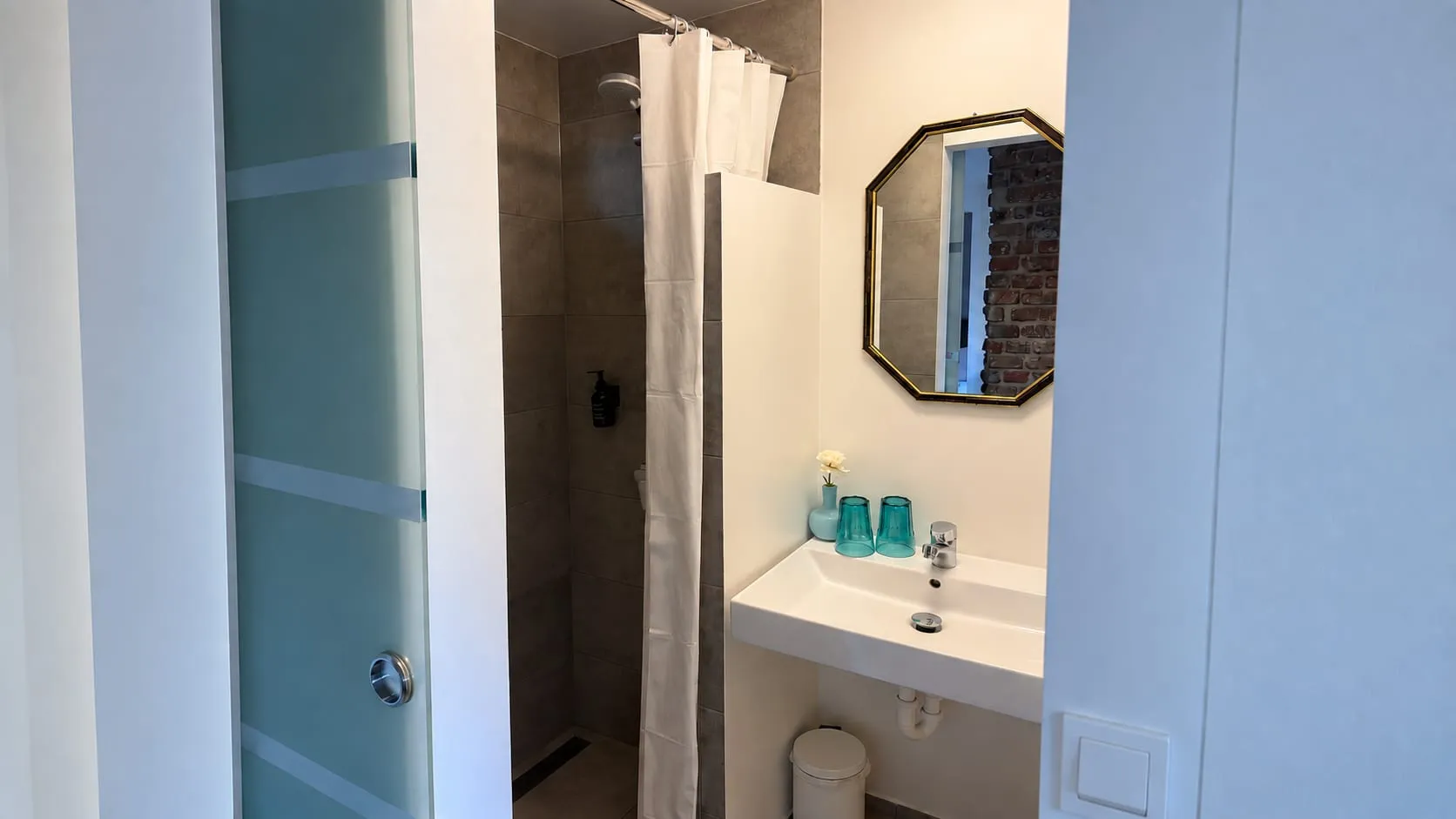 Badezimmer mit Dusche und achteckigem Spiegel, Blick durch die Schiebetür